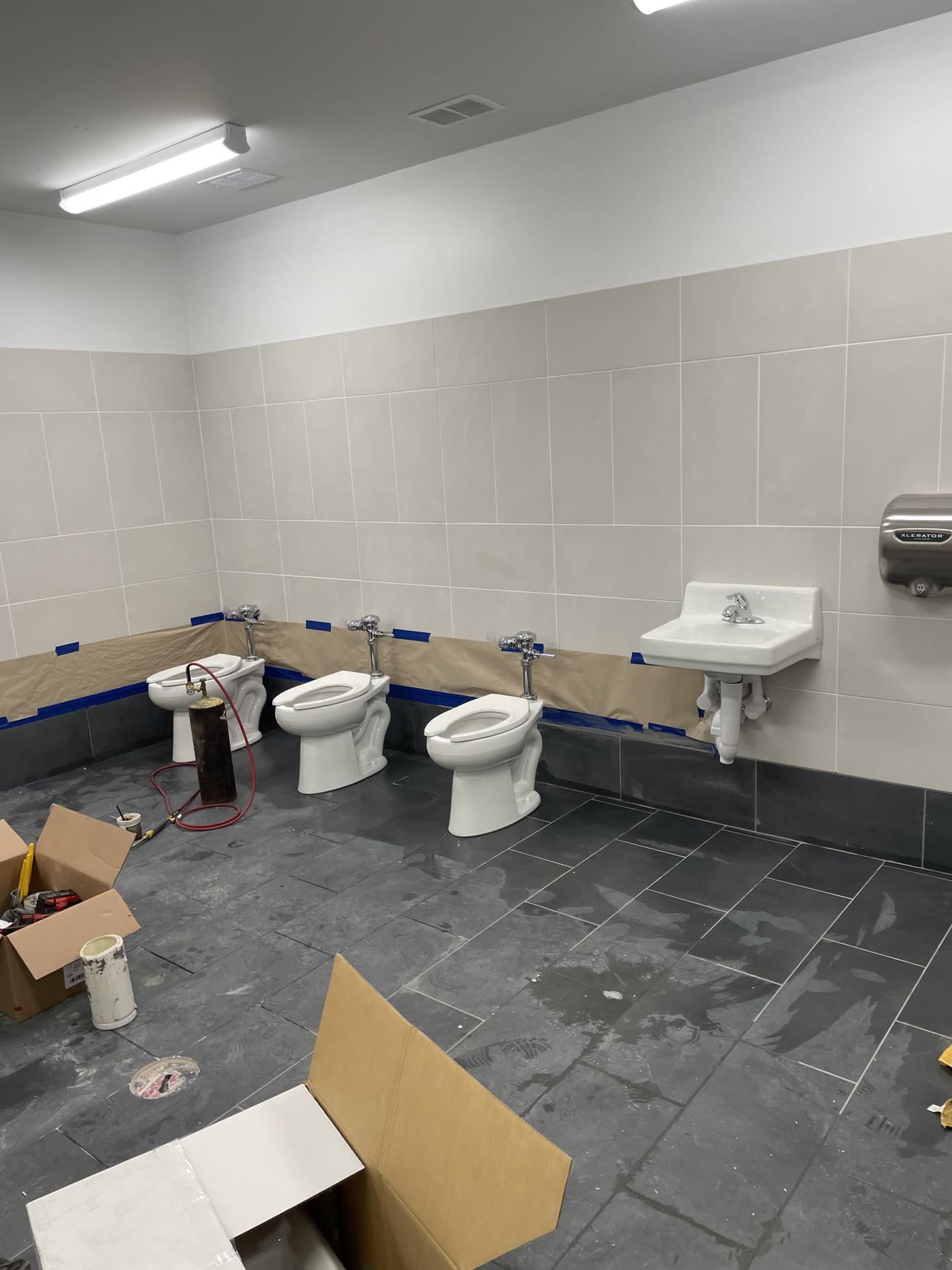 Three commercial toilets set on a tiled restroom floor during trim