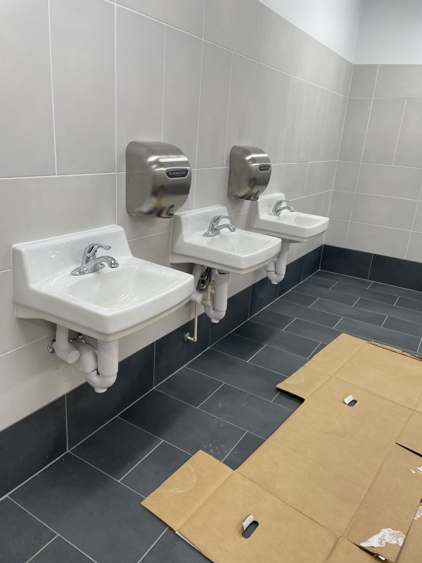Three wall-hung restroom sinks with chrome faucets and hand dryers