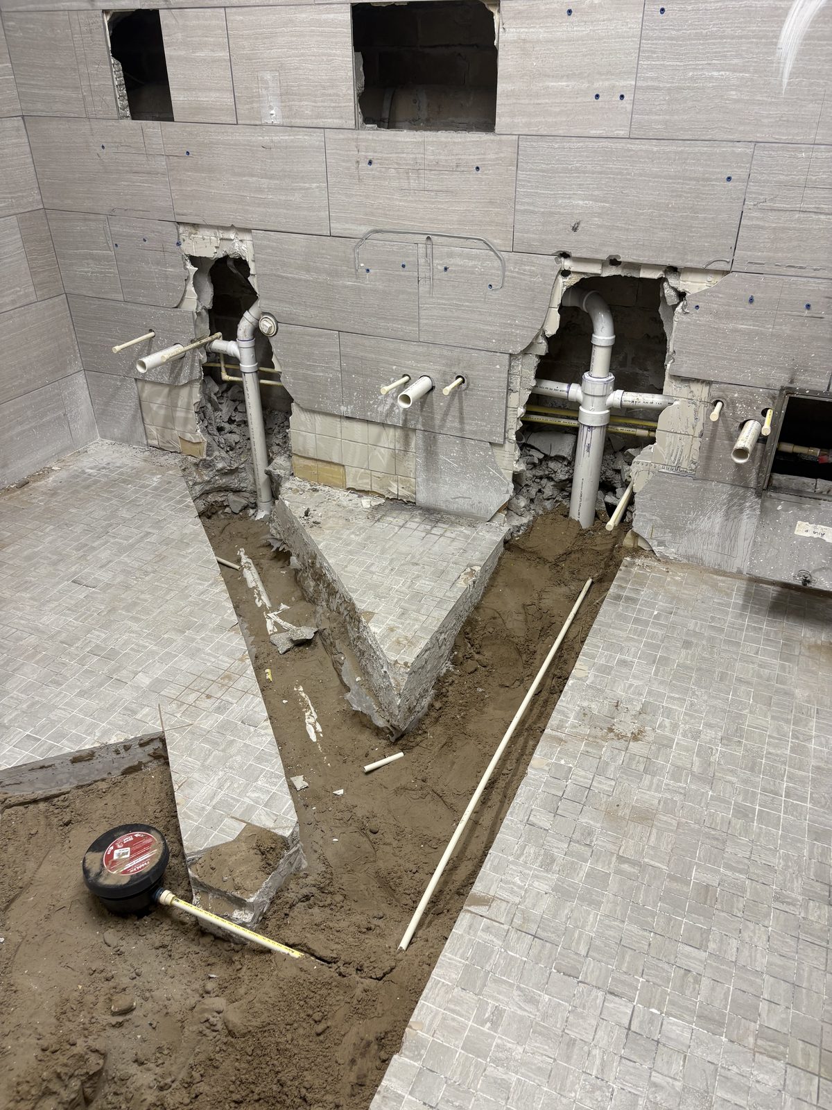 Commercial restroom wall and floor opened with PVC drain lines in the trench