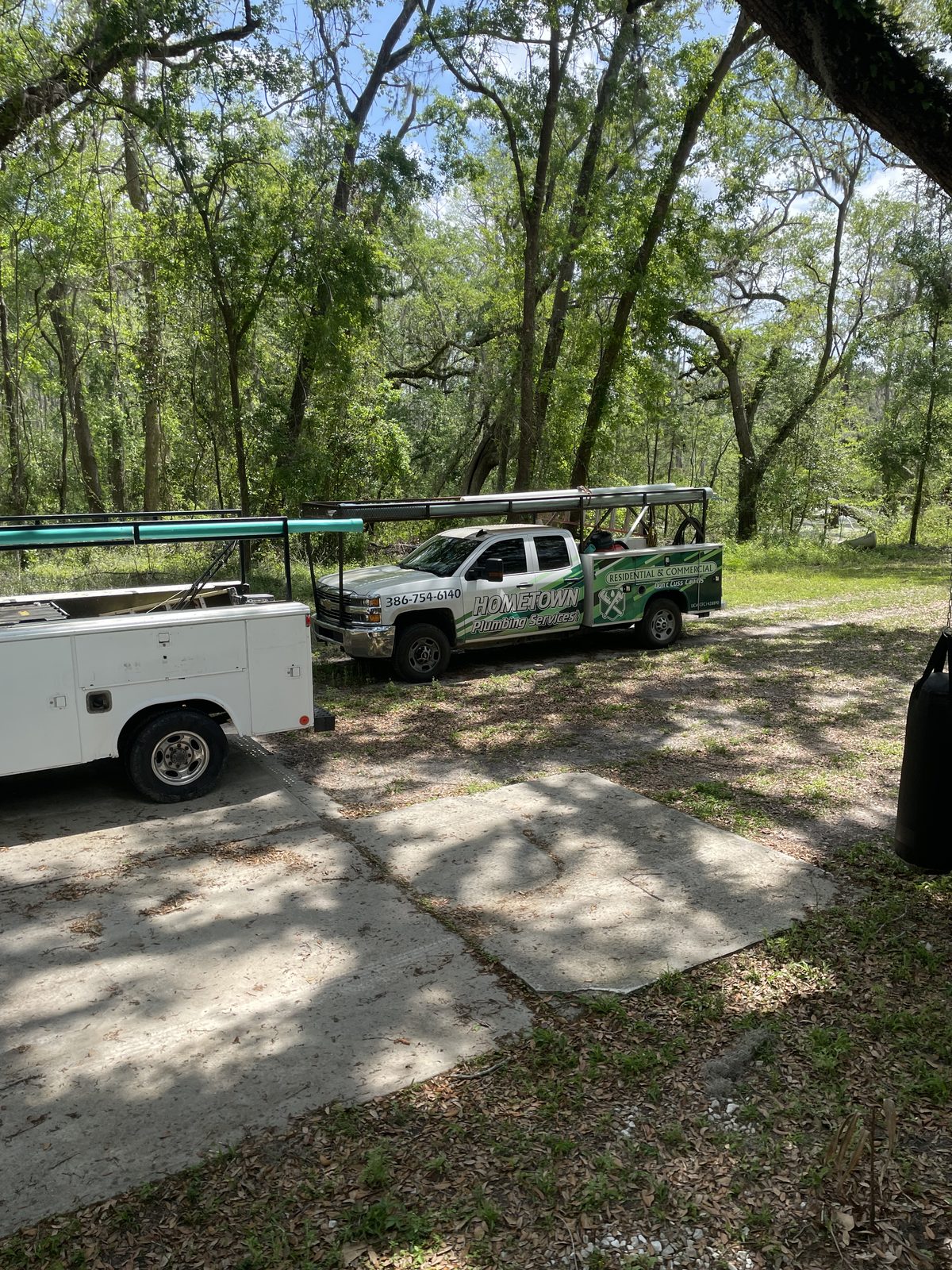 Hometown Plumbing service trucks parked under live oaks, 386-754-6140 on the door